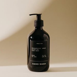 A black pump bottle with a label that reads "PRESTON - HAND WASH 16OZ Moisturizing Olive Oil Hand Wash Amber, Sulfate-Free, Made in USA." The bottle is standing against a neutral background.