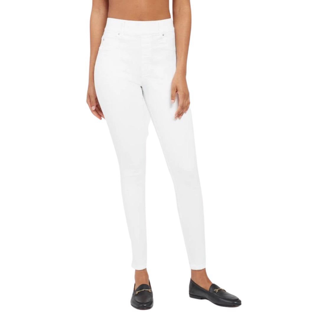 A person wearing the SPANX - SKINNY JEAN, which is a pair of high-waisted white skinny jeans crafted from stretch denim, and black loafers stands against a plain white background. The image focuses on the lower body, highlighting the jeans' high-rise coverage and footwear.