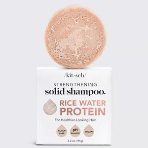 A box of KITSCH RICE WATER PROTEIN SHAMPOO BAR rests on a tiled surface. The packaging emphasizes key features including cruelty-free, vegan, zero waste, color-safe, and made with recycled paper. Perfect for those seeking to repair damaged hair, a customer review by Joni W. reads, "My hair definitely feels fluffier today.