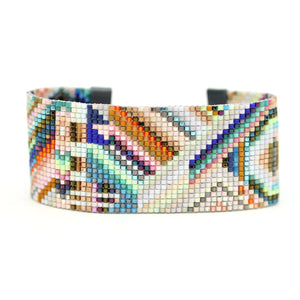 The JULIE ROFMAN - FLORES CUFF from JULIE ROFMAN JEWELRY is a vibrant beaded cuff adorned with a geometric abstract design crafted from handwoven glass Delica beads. It features a gray leather strap and a small metallic buckle, showcasing an array of pastel and bright colors.