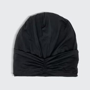 Packaging for the SLEEP BEANIE WITH SATIN LINING by KITSCH. The primarily white box features a cut-out displaying the black beanie inside. It advertises "Bye Bye Bedhead" and highlights that it’s "Seriously, SO SOFT!" Designed to prevent hair breakage, a small image shows a person wearing the jersey bonnet.