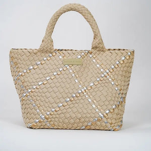 A person in a beige sleeveless top and ripped blue jeans holds a Parker & Hyde - Beige Metallic Woven Tote Bag, featuring a checkered design with subtle white accents and two handles. The background is plain light gray.