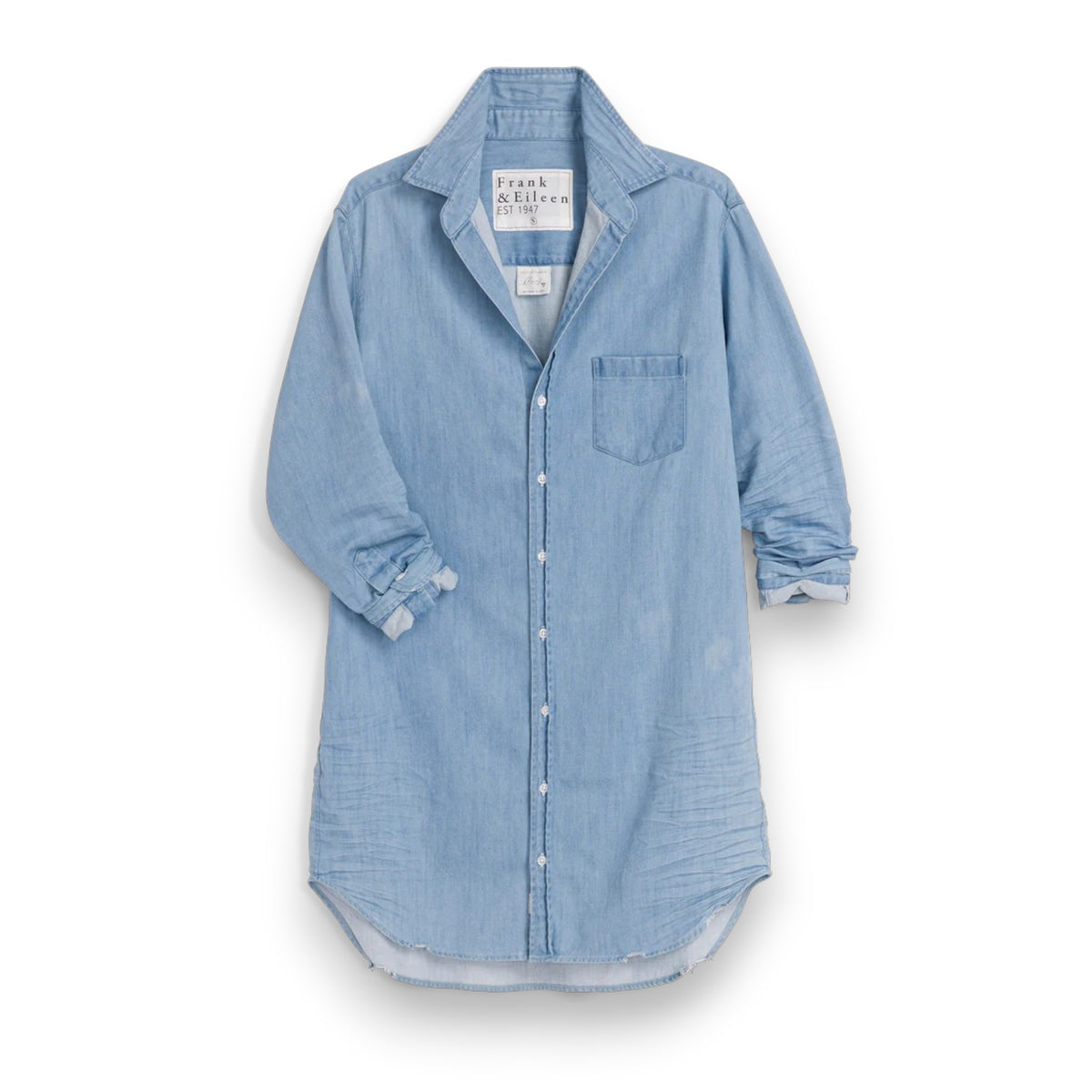 A woman smiles outdoors in the FRANK &amp; EILEEN Mary Classic Shirtdress in Famous Denim Classic Wash, standing amid garden greenery and patio furniture.