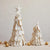 Two CREATIVE COOP HANDMADE WOOD FELT CHRISTMAS TREE decorations, each topped with a star and adorned with small gold beads, are displayed on a neutral surface. The larger tree showcases layered petals, while the smaller one mirrors this design. Festive gold jingle bells and ornaments are scattered around them to enhance the holiday ambiance.