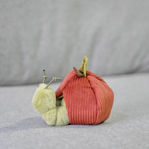 The LAMBWOLF COLLECTIVE - APPLE DOG TOY by LAMBWOLF COLLECTIVE features a furry plush caterpillar peeking out from a cozy, red, corduroy crinkly apple, set against a soft, gray background. The caterpillar includes wire antennae for added fun. This interactive dog toy is ideal for engaging playtime.