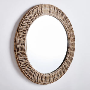 The KYLAN ROUND MIRROR by NAPA HOME AND GARDEN, featuring a large gauge woven rattan design and a wide, wicker frame in light brown, adds a natural and rustic touch to your décor. This exquisite addition to your bedroom or open-concept space beautifully reflects any plain, white background.