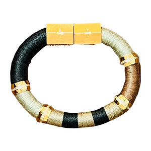 Introducing the HOLST + LEE - COLORBLOCK BRACELET by HOLST & LEE: a circular, multicolored accessory featuring sections of black, beige, and brown materials. This stunning bracelet is embellished with gold rings and a rectangular gold-plated magnetic clasp, seamlessly combining metallic elements with soft textured segments crafted from pearl cotton thread.