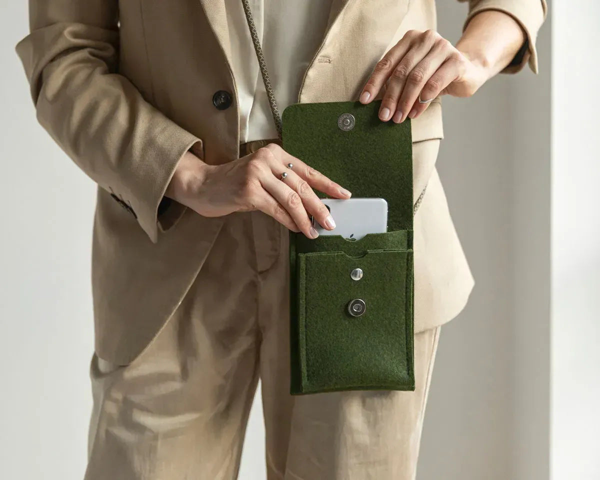 A person in a loose gray shirt and taupe pants carries the WOOLBERRY WOOL FELT PHONE BAG—a pink crossbody with a flap and silver chain—over their shoulder, showing only their torso and part of their arms.