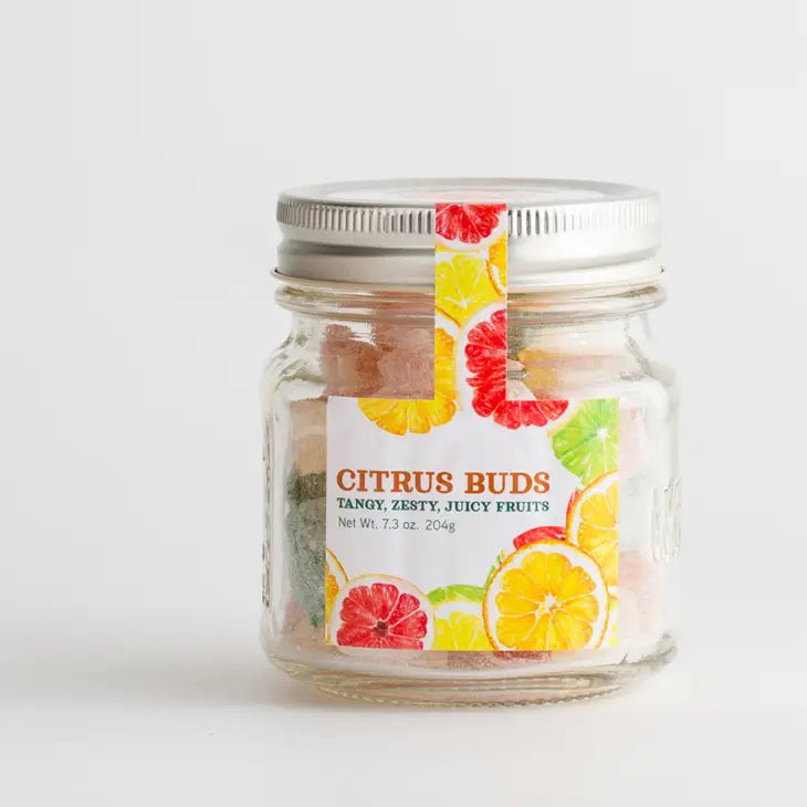 A clear mason jar with a silver lid containing colorful, citrus-flavored hard candies. The label reads "BUTTERFIELDS - CITRUS BUDS" and "Tangy, Zesty, Juicy Fruits" with illustrations of oranges, lemons, and grapefruits. The jar's net weight is 7.3 oz (204 g).