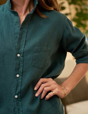 The FRANK & EILEEN's Eileen Relaxed Button-Up Shirt in Washed Linen Forest is displayed in the image. This green, long-sleeve shirt features a front pocket and a relaxed fit with bust-flattering button placement. The sleeves are rolled up to mid-forearm and all buttons are fastened, exuding California effortlessness against a plain white background.