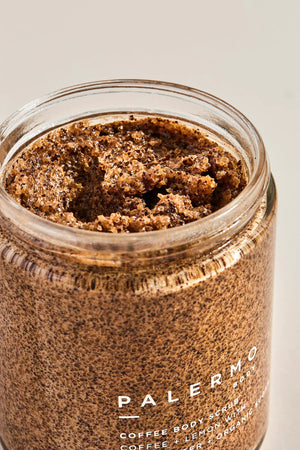 A jar of PALERMO BODY - COFFEE & LEMON BODY SCRUB is shown against a white background. The organic coffee scrub, featuring lemon, shea butter, moisturizing coconut oil, and organic sugar, comes with a black lid. The label details the product information and the quantity is 8.5 oz / 240 g.