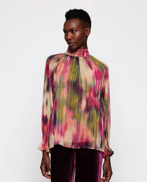 A person with short hair is wearing the MIRTO 1956 Multicolor Chiffon Ikat Print Blouse, a long-sleeve, high-neck top adorned with a vibrant abstract tie-dye pattern in shades of pink, green, and cream. This chiffon blouse by MIRTO 1956 features smocked cuffs on its raglan puff sleeves. The person is shown from the back against a plain white background.