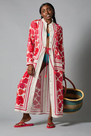 A barefoot person stands against a gray backdrop wearing the HOPE FOR FLOWERS - BAND COLLAR SHIRTDRESS, which features a cream background with vertical stripes, long red florals, a cinched waist, and long sleeves.