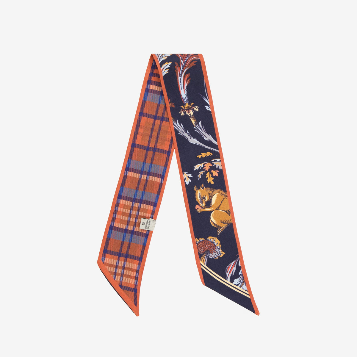 A hand wears the INOUI EDITIONS ROCOCO SQUIRREL SILK RIBBON by INOUI, its red, navy, and beige squirrel and foliage motif adding elegance to light beige pants and a black top.