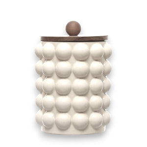 The CANISTER WITH RAISED DOTS & ACACIA LID by CREATIVE COOP is a beige ceramic stoneware container featuring a unique, bubble-like texture and an acacia wood lid with a spherical knob. Ideal for kitchen storage, this stylish and functional piece blends modern design with decorative flair.