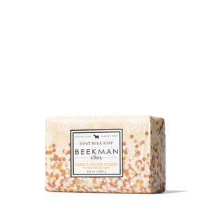 A bar of BEEKMAN - 9OZ. HONEY & ORANGE BLOSSOM BAR SOAP from the BEEKMAN - STA ELEMENTS line is wrapped in decorative paper adorned with white and orange floral patterns. The label highlights that it is free from sulfates and parabens, featuring an illustration of a goat above the brand name, assuring you it's a moisturizing soap you can trust.