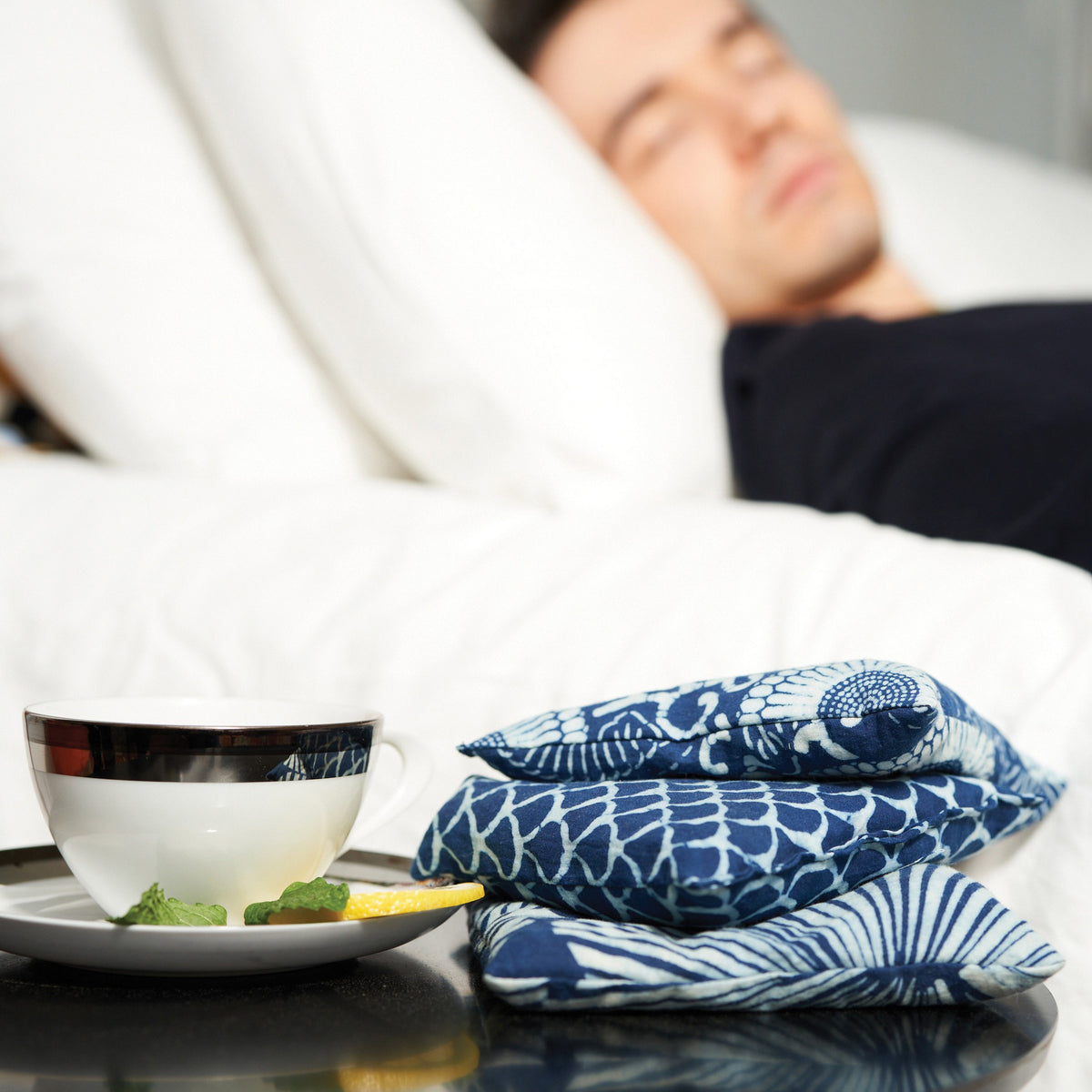 Three square pillows in blue and white patterns—a geometric wave, a radial fan motif, and circular flower-like shapes adorned with leafy details—ideally complement the use of BAUDELAIRE&#39;s Chamomile Sleep Sachets by infusing relaxation into your sleep sanctuary.