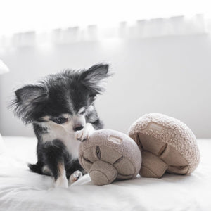 A small, plush button mushroom toy from LAMBWOLF COLLECTIVE. The cap is covered in a fuzzy, textured fabric, while the stem and gills are made from a smoother material in a matching beige color. Designed by LAMBWOLF COLLECTIVE to look cute and cuddly, this washable pet toy is perfect for both playtime and snuggles.