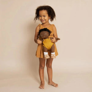 A DINKUM DOLL from OLLI ELLA USA features soft brown hair and comes dressed in a white knit romper paired with brown shoes. This charming doll has an embroidered face with brown eyes, a small nose, and a gentle smile. Its posable body makes it perfect for imaginative playtime, and it is posed standing upright.