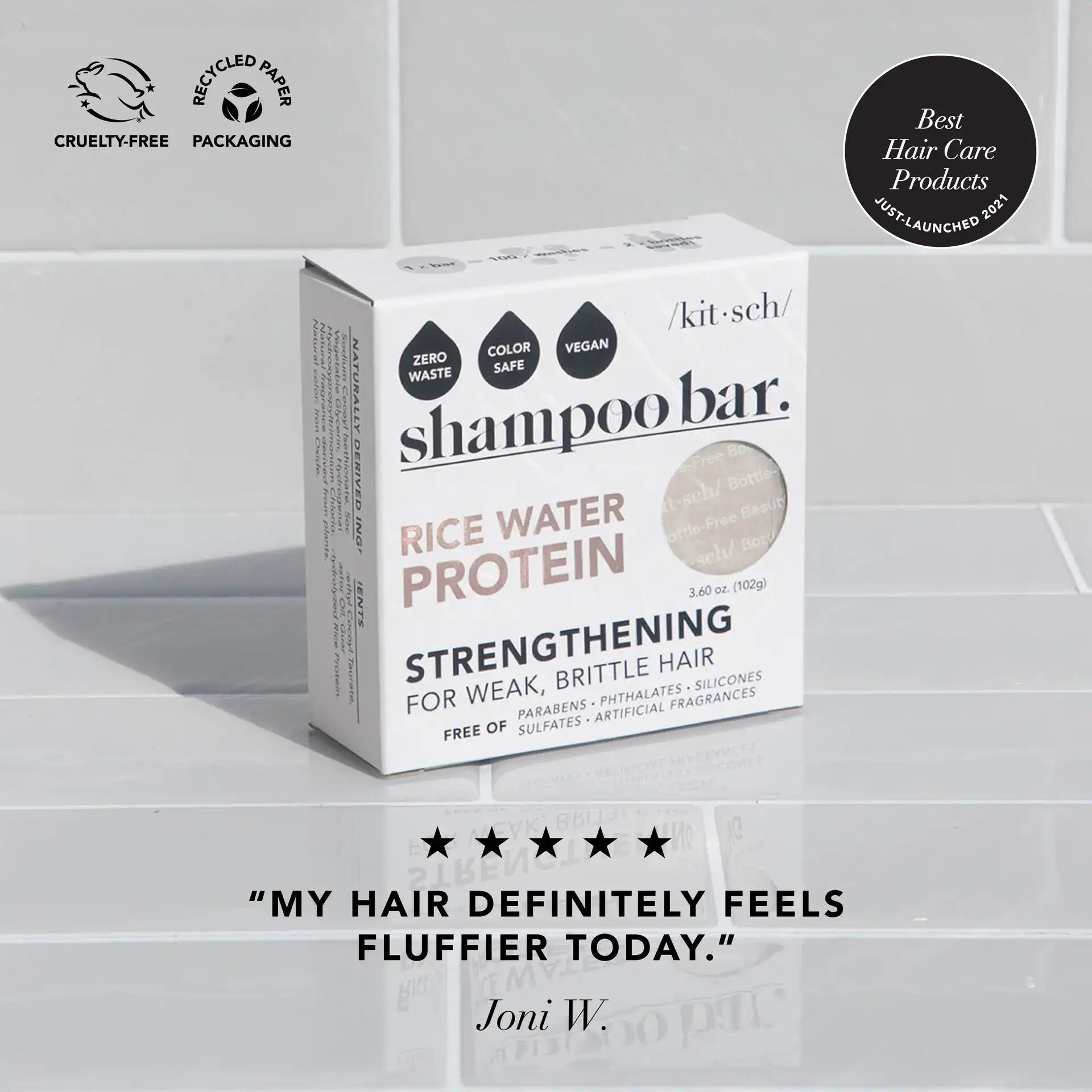 A box of KITSCH RICE WATER PROTEIN SHAMPOO BAR rests on a tiled surface. The packaging emphasizes key features including cruelty-free, vegan, zero waste, color-safe, and made with recycled paper. Perfect for those seeking to repair damaged hair, a customer review by Joni W. reads, "My hair definitely feels fluffier today.