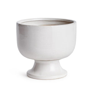 The ALBIE FOOTED CACHEPOT by NAPA HOME AND GARDEN is a white, ceramic pedestal bowl featuring a smooth, shiny white glaze with a slightly rounded top edge. Elevated on a short, cylindrical base, its traditional shape and minimalist design make it an ideal centerpiece. Subtle crackle patterns on the surface add texture and charm.