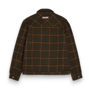 The AMUNDSEN SPORTS Wool Jacket is a unisex dark plaid overshirt with a brown and mustard check pattern, long sleeves, buttoned cuffs, and a small red, white, and blue striped tag near the back collar. Laid flat, viewed from behind.