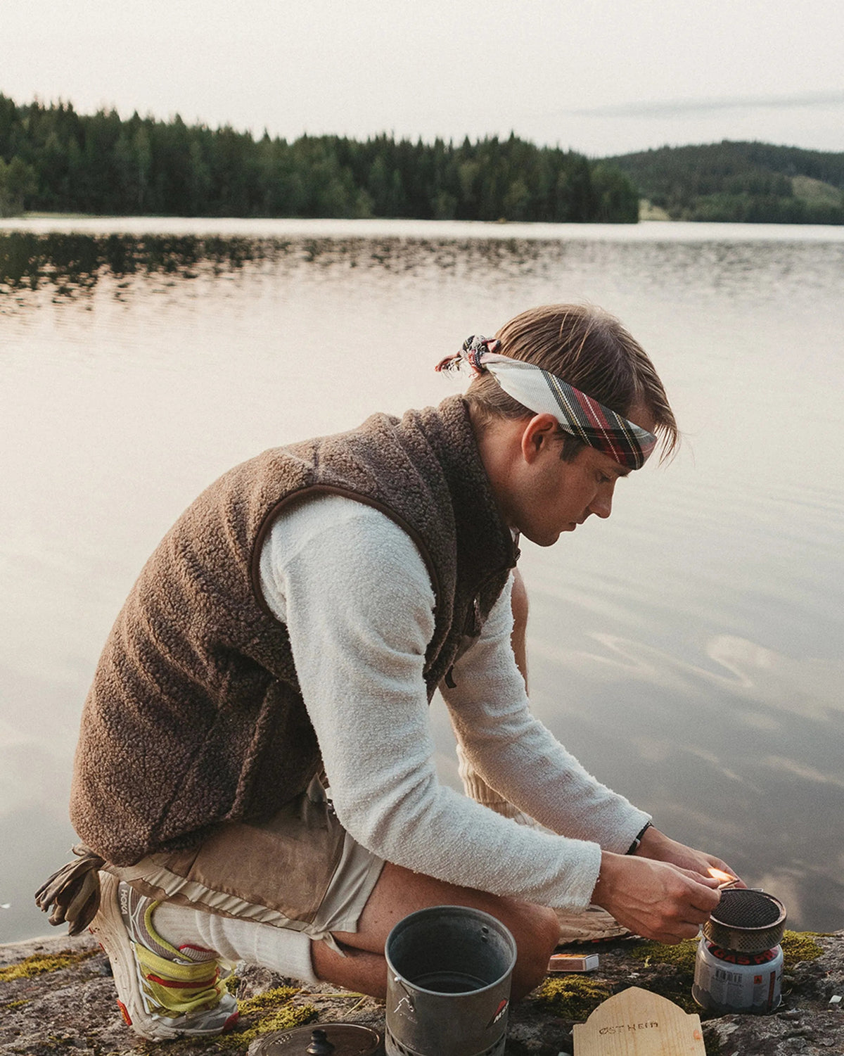 The AMUNDSEN SPORTS Heroes Fleece Vest in Cowboy features a brown sherpa wool texture, front zipper, high collar, two large side pockets, and a chest pocket with a tan patch for warmth and style.