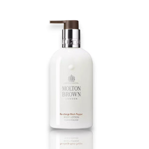 A dollop of smooth, white MOLTON BROWN - BLACK PEPPER BODY LOTION is spread on a white surface with a reflective sheen. Infused with notes of vetiver and black pepper, the lotion has a glossy texture that tapers off with slight ridges, giving it a fluid and fresh appearance.