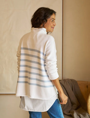 A woman with long dark hair wears a Monterey Rolled Funnel Neck Stripe Sweater from FRANK & EILEEN. The sweater, made of machine-washable Italian cotton, features light gray stripes on the back. She layers it over a white shirt and gazes to the side in a softly lit neutrally toned room.