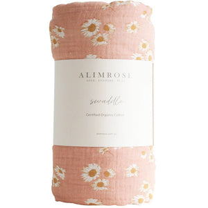 An ALIMROSE Muslin Swaddle made from 100% organic cotton. The pink swaddle features a charming pattern of white daisies, and the label includes the brand name and product details. It's conveniently machine washable.