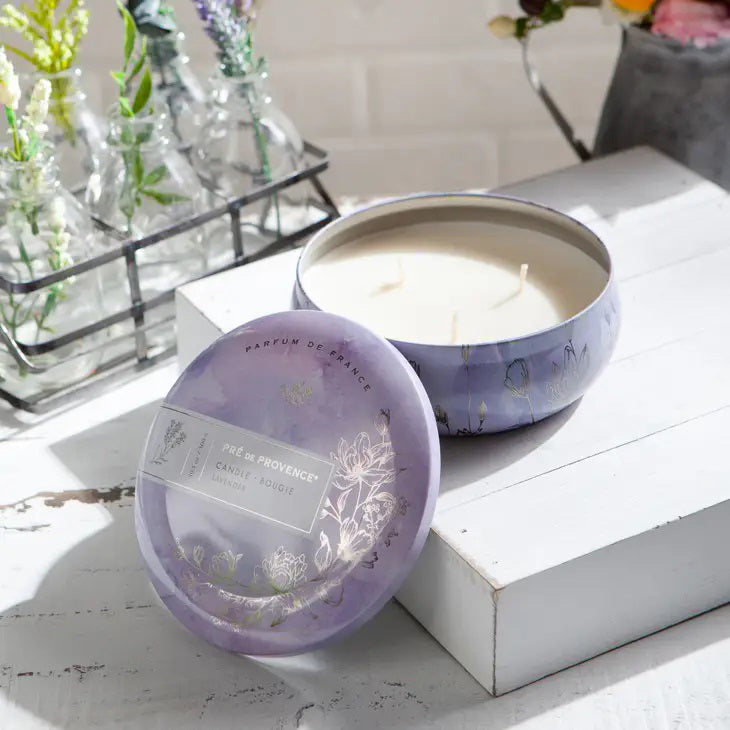 A round 3 Wick Candle - Lavender from European Soaps, LLC, featuring delicate floral illustrations in purple and white tones. The label includes &quot;Pré de Provence,&quot; &quot;Candle,&quot; and &quot;Lavender,&quot; along with a &quot;Parfum de France&quot; inscription and an image of a bird, perfect for enhancing your home ambience.