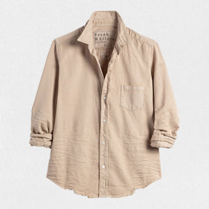 A long-sleeved, sand-colored button-up shirt from Frank & Eileen hangs against a light grey textured background. The shirt, known as the Barry in Famous Denim Sand and a closet essential, features a single chest pocket, slightly wrinkled fabric, and rolled-up sleeves. The label visible inside the collar reads "Frank & Eileen EST 1947.