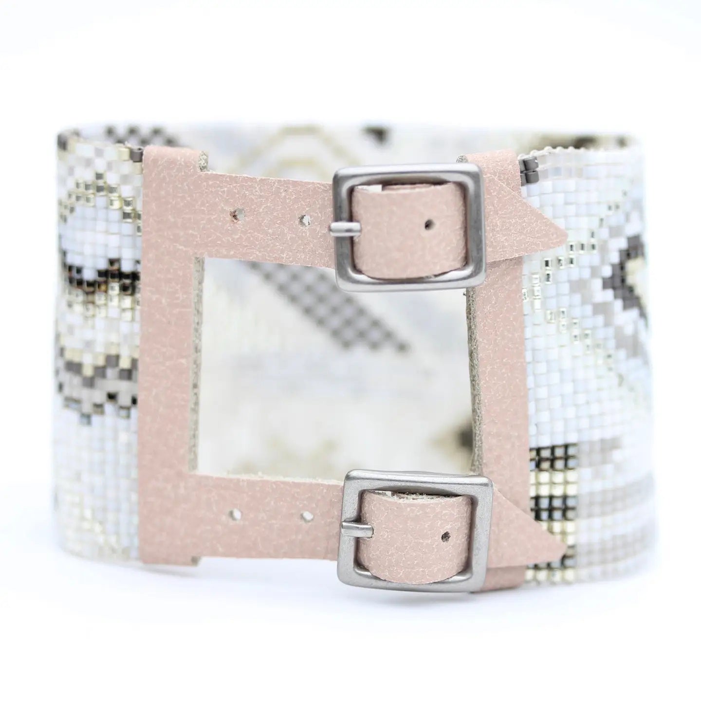 The JULIE ROFMAN - QUARTZ CUFF by JULIE ROFMAN JEWELRY is a wide bracelet showcasing a handwoven, beaded geometric pattern in neutral tones. It features two beige leather straps with silver buckles and an open rectangular center for a distinctive touch.