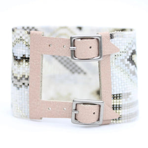 The JULIE ROFMAN - QUARTZ CUFF by JULIE ROFMAN JEWELRY is a wide bracelet showcasing a handwoven, beaded geometric pattern in neutral tones. It features two beige leather straps with silver buckles and an open rectangular center for a distinctive touch.