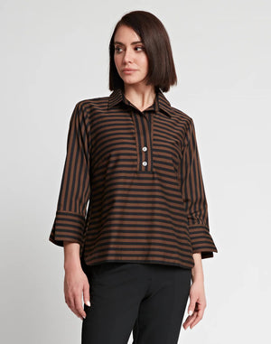 A woman with shoulder-length dark hair wears the HINSON WU - AILEEN 3/4 SLEEVE STRIPE GINGHAM COMBO SHIRT, a black and beige striped blouse featuring a small collar and a partial zip at the front. She pairs it with black pants and stands against a plain white background, one hand in her pocket.