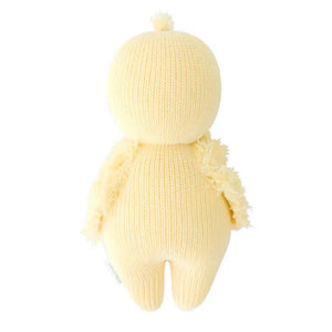 A soft, knitted yellow plush toy named "CUDDLE + KIND - HANDMADE BABY DUCKLING" by the brand CUDDLE & KIND, featuring a round head and body and viewed from the back. This charming toy has small wings and a tuft of 100% cotton yarn on its head, resembling a hand-knit baby chick while providing fair trade income to artisans.