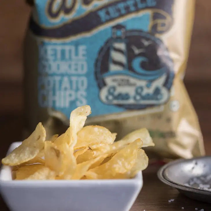 A bag of CAROLINA KETTLE - SEA SALT CHIPS 5OZ by 1 IN 6 SNACKS. The packaging is brown and beige with blue and black text. The bag mentions it contains 5 ounces (142g) of crispy, certified-quality kettle chips and proudly highlights that they are gluten-free and kosher.