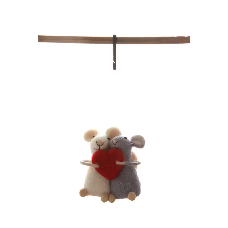 The WOOL FELT MICE WITH HEART ORNAMENT from CREATIVE COOP features a pair of wool felt mice, one in white and the other in gray, holding a red heart ornament together beneath a slender horizontal brown beam against a plain white background.