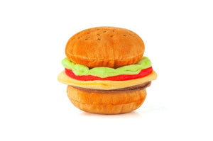 The AMERICAN CLASSIC BURGER by PLAY PET LIFESTYLE, a plush toy shaped like a classic American hamburger, is pictured against a white background. This foodie delight features a soft, brown bun with sesame seeds, green lettuce, a slice of red tomato, yellow cheese, and a brown burger patty.