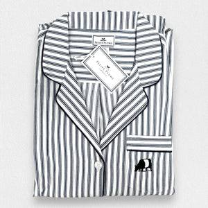 The FEARRINGTON LIFESTYLE COLLECTION - MENS TWILL NAVY FRENCH TICKING PAJAMAS by PETITE PLUME is neatly folded and displayed. This striped pajama set, made from the finest quality cotton, features white and navy blue vertical stripes in a traditional French ticking design with a small embroidered sheep on the chest pocket. It has a collar, buttons, and an attached hang tag with branding.