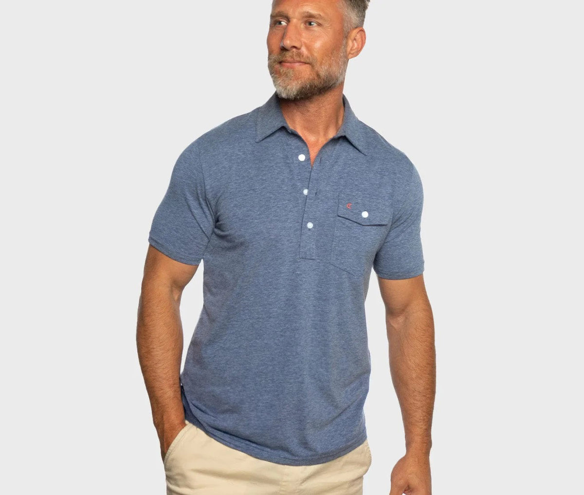 A man with short gray hair and a beard wears the CRIQUET - PERFORMANCE PLAYERS SHIRT IN MIDNIGHT, featuring classic fit and moisture-wicking fabric, paired with beige pants, standing against a plain light background.