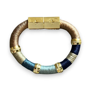 Introducing the HOLST + LEE - COLORBLOCK BRACELET by HOLST & LEE: a circular, multicolored accessory featuring sections of black, beige, and brown materials. This stunning bracelet is embellished with gold rings and a rectangular gold-plated magnetic clasp, seamlessly combining metallic elements with soft textured segments crafted from pearl cotton thread.