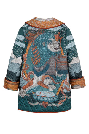 A person wears the SABINA SAVAGE - THE SNOW LION QUILTED JACKET from SABINA SAVAGE ENGLAND, featuring a colorful, intricately designed nature-themed pattern with trees, sky, and animals. Reminiscent of a reversible silk twill jacket, it features a wide collar, contrasting orange inner lining, and large pockets. The person is shown from the shoulders down.