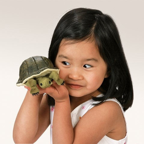 A FOLKMANIS - MINI TURTLE FINGER PUPPET from FOLKMANIS PUPPETS nestled on a person's hand, with its dark shell, light green limbs, and black claws gives a realistic effect. The human hand underneath supports it, making it look like the turtle is ready to play peek-a-boo.