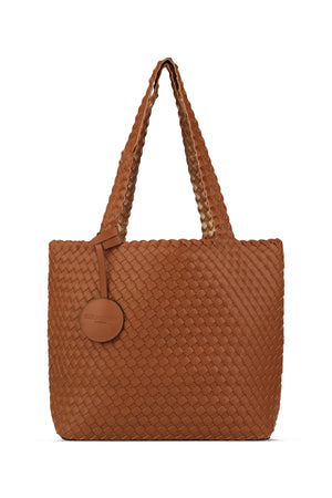 The WOVEN REVERSIBLE TOTE BAG by LINES OF DENMARK is a white tote featuring two shoulder straps and a circular faux-leather tag on one strap. This shopper showcases a textured, interlaced pattern and reversible design, providing stylish and elegant dual styling options. The image background is plain white.