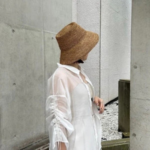 The WYETH HATS - THE TALI is a brown hand-crocheted raffia straw hat featuring a wide brim, showcased against a plain white background.