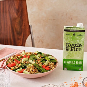 A carton of KETTLE & FIRE - ORGANIC VEGETABLE COOKING BROTH with a green label. The text highlights "Organic Ingredients" and "No Preservatives." The front features the product name and an illustration of vegetables. It states "New Look" at the top and specifies a net weight of 32 fl oz (907g), perfect for cooking flavorful meals.