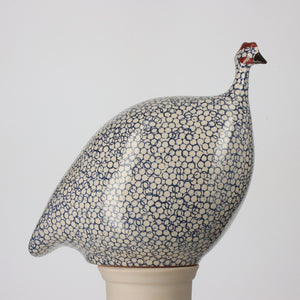 This stunning LES CERAMIQUES DE LUSSAN piece, the LES CERAMIQUES DE LUSSAN - LARGE CERAMIC FRENCH GUINEA IN WHITE SPOTTED COBALT, features a guinea fowl with a speckled blue and white pattern reminiscent of South of France pottery. The bird stands on a pale, unglazed base, and its head is detailed with red and black accents, reflecting the unique artistry of Heidi Caillard's creations against a plain white background.