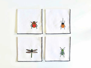 Four EMBROIDERED INSECT COASTERS from DOT AND ARMY are displayed in a 2x2 grid on a light surface. Each coaster, crafted in Georgia, features colorful embroidered insects: a red and black ladybug in the top left, an orange and black beetle in the top right, a green dragonfly in the bottom left, and a green bug in the bottom right.