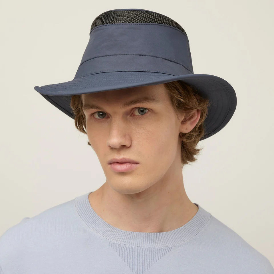 The TILLEY - AIRFLO MEDIUM BRIM LTM5 by TILLEY is a blue hat made from recycled nylon, featuring a black mesh ventilation band around the crown and metal eyelets, shown on a plain light gray background.